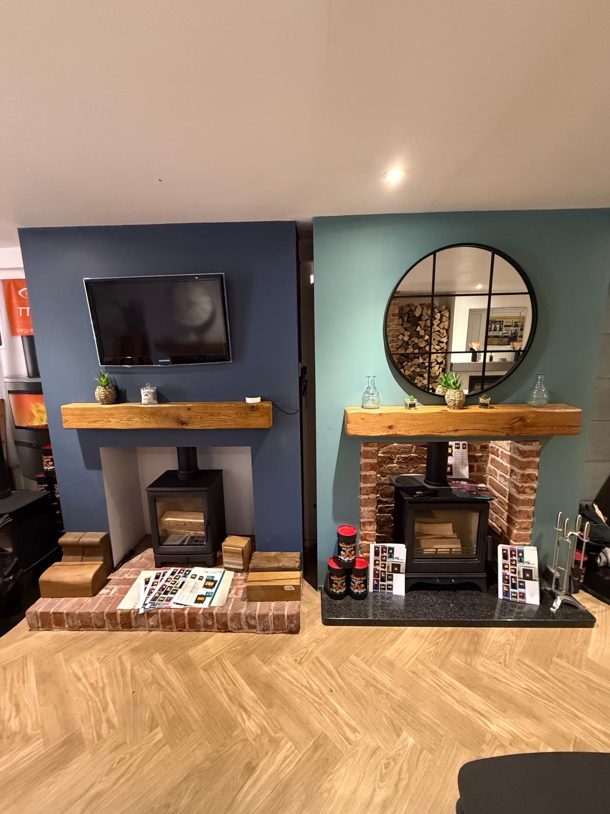 A pair of stove displays against blue and teal walls with rustic oak beam mantels.